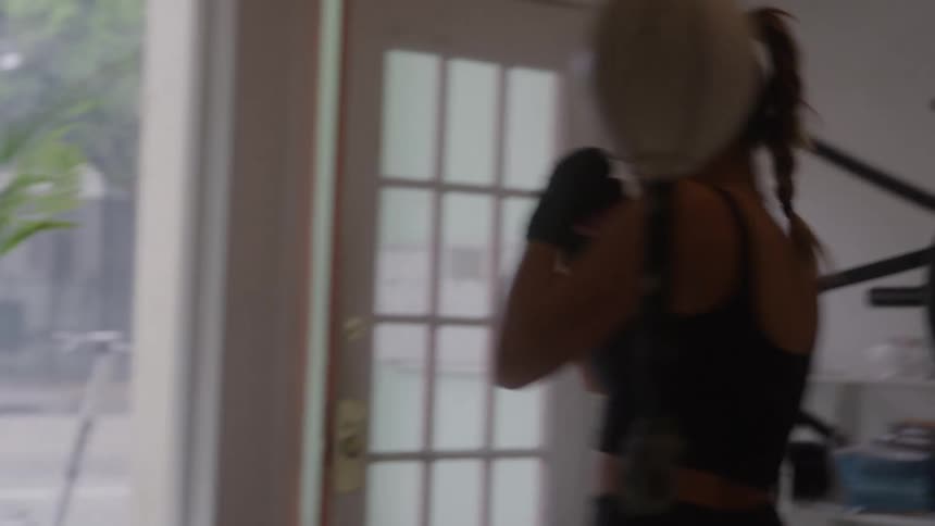 A woman in a black sports top throws quick punches near a glasspaneled door looking focused and energized