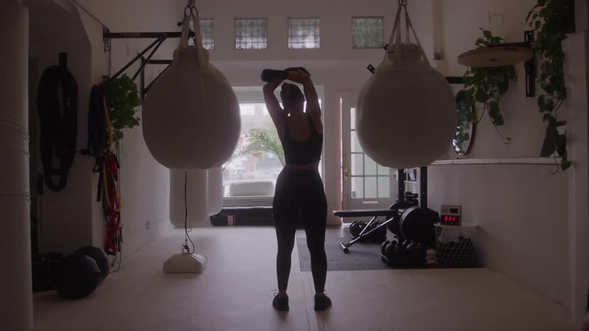 Woman stretches while standing in a gym during the daytime