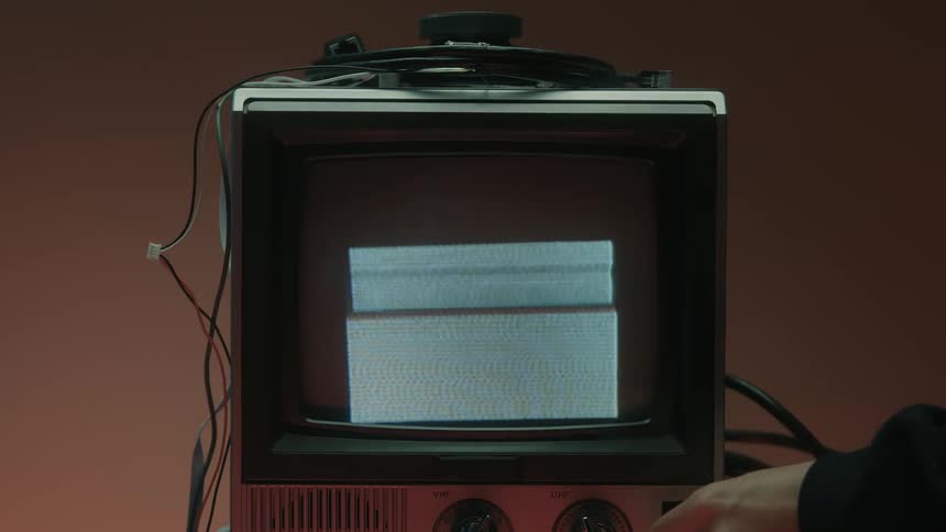 Hand turns dial on old tv showing static and colored lines