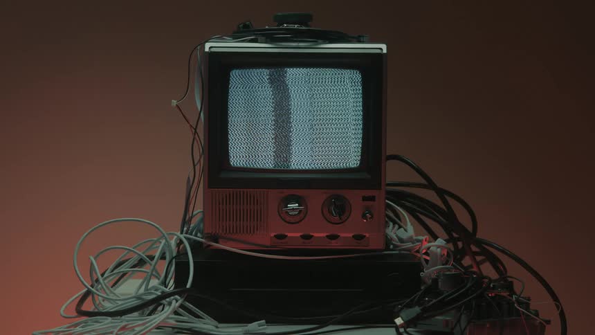 Old television turned on shows static noise surrounded by scattered cables