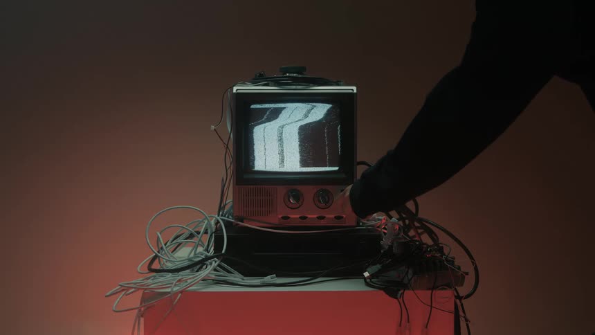 Man turns off a small television sitting on a small table surrounded by electric cables