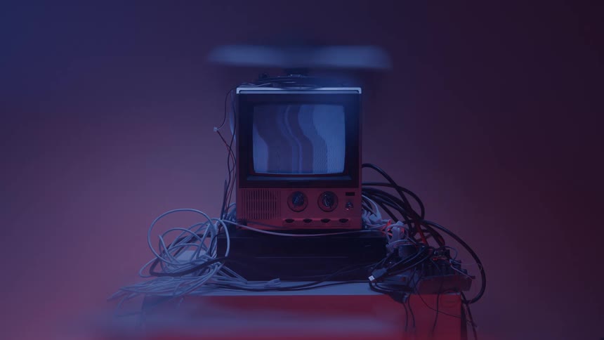 Hand turns a knob while powering on an old television surrounded by cables