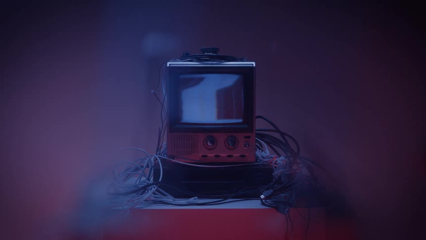 Hand turns a knob while powering on an old television surrounded by cables