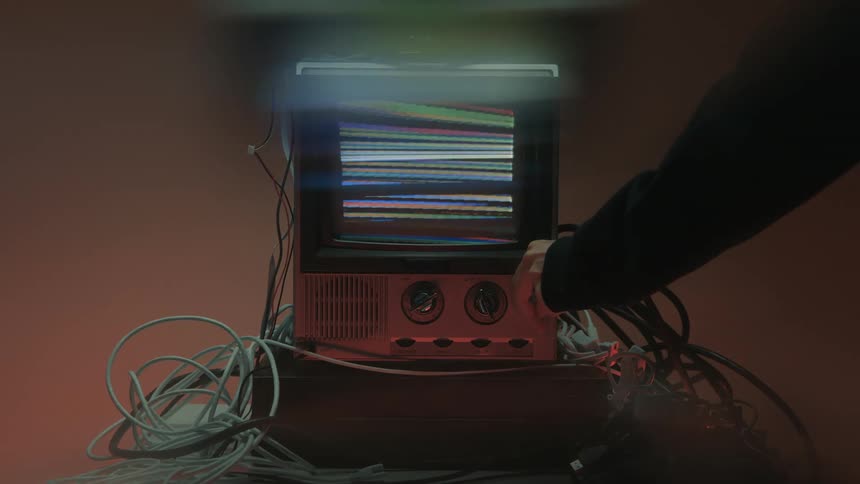 Person turning off a retro television surrounded by cables