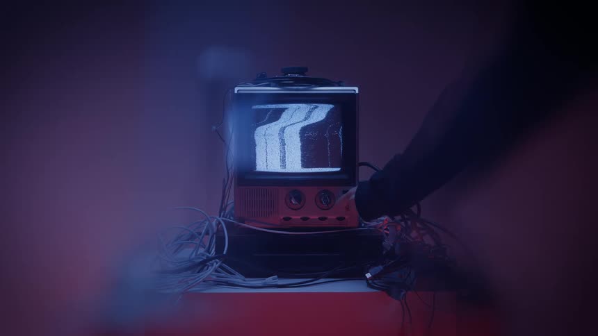 A person turns off a connected electronic display device on a table in a red lit room