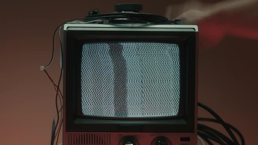 A small television displaying a visual static pattern while a human hand gives a slap in the back of the television