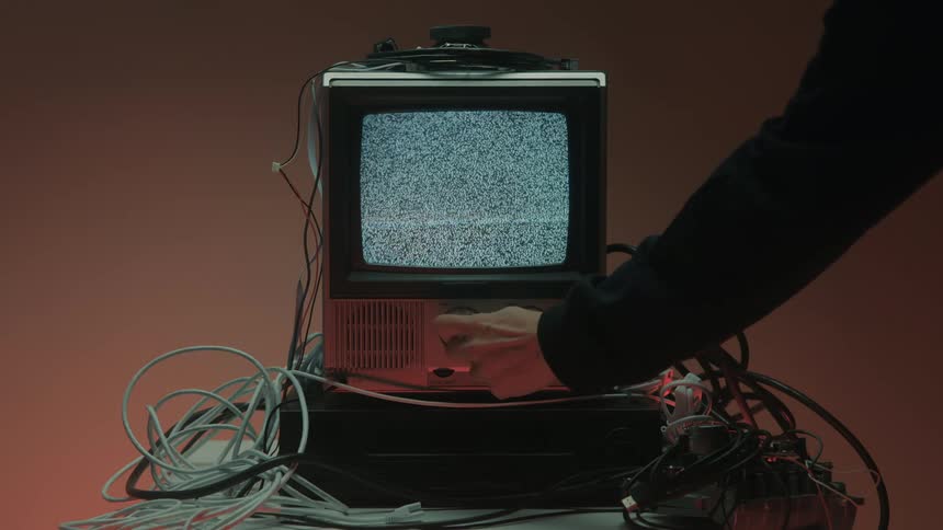 Hand turns a knob while changing the channel on an old television with static noise