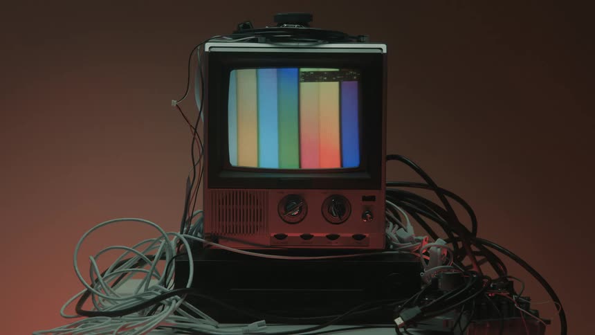 Screen of a small television surrounded by cables shows the smpte color bars