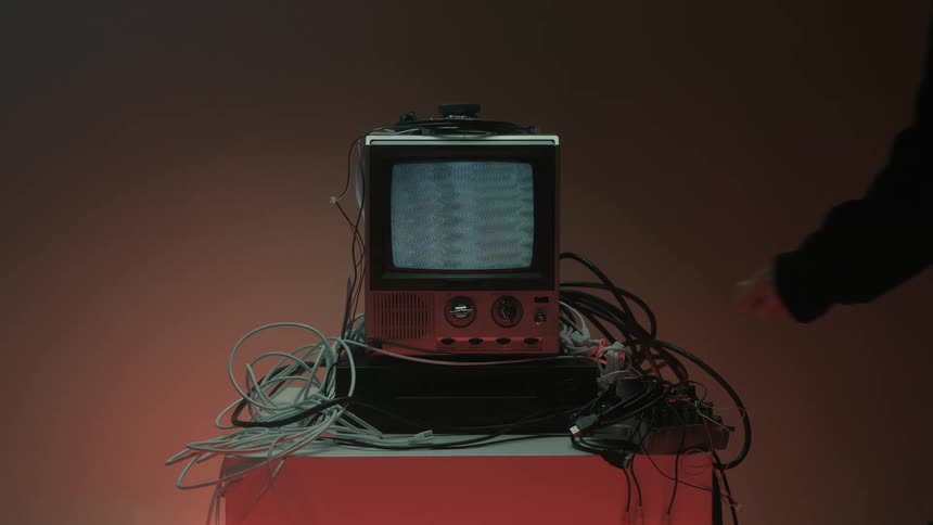 Hand turns the knob of a retro television surrounded by cables to switch it on
