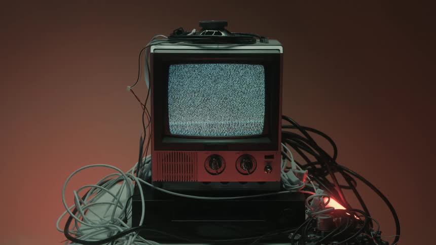 Small television sitting on a media player and surrounded by cables displays signal static