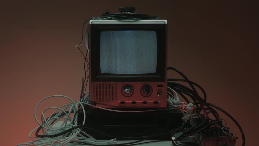 Person turning on an old television with no signal surrounded by cables