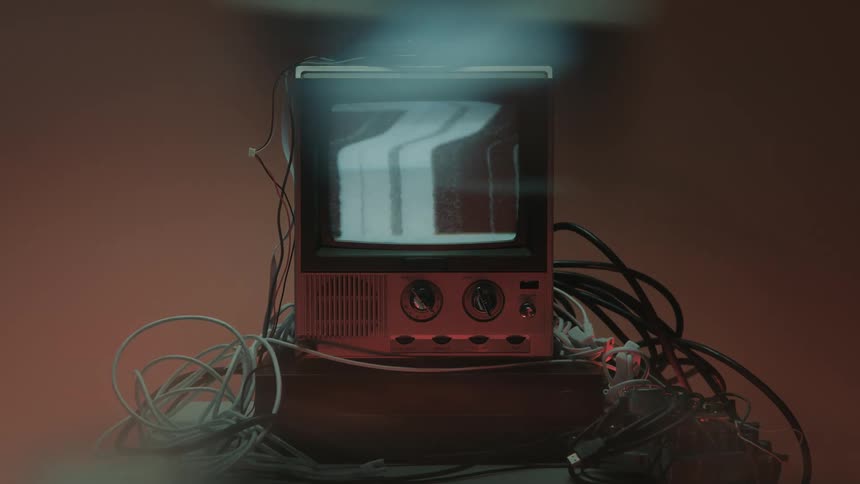 A television set turned off with a lot of cables next to it with a human hand reaching to turn it on