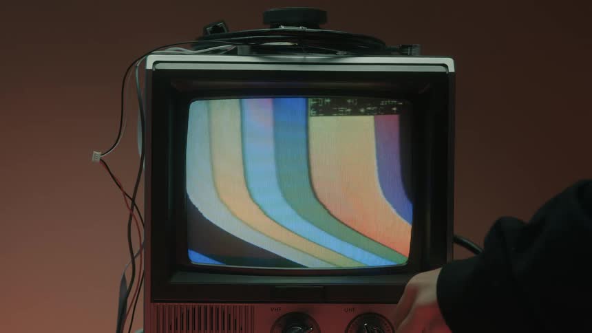 An antique television displaying a color bar test pattern is turned off by a human hand manipulating a control knob causing the screen to go black