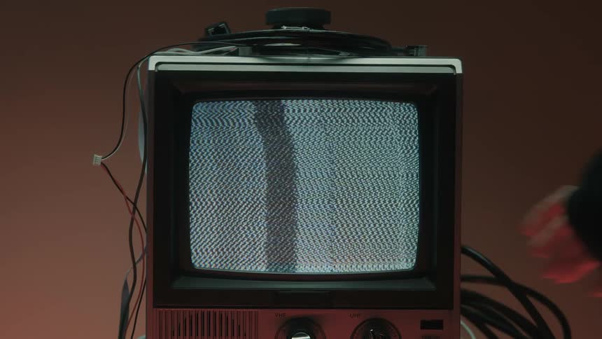 Man taps a small television trying to fix a screen showing signal static