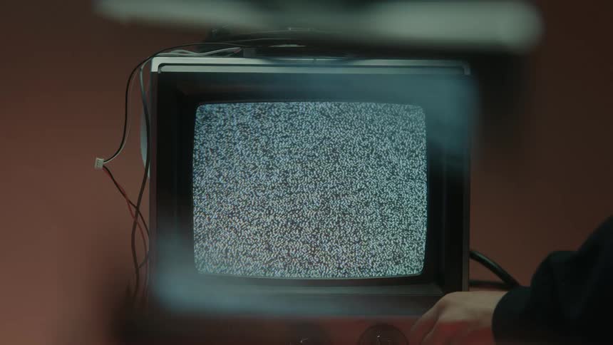 Hand turns a knob while turning off an old television displaying static on the screen
