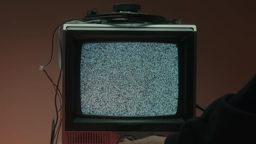 Old television turned on displays static noise as a hand adjusts the dial