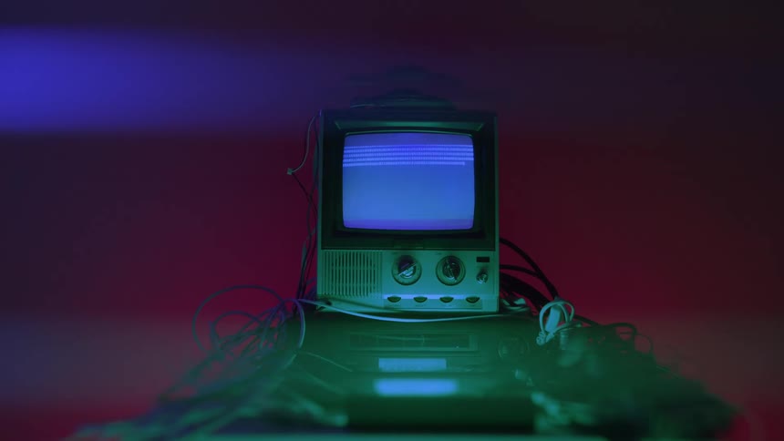 Old television turned on with a blue screen surrounded by cables under neon lights