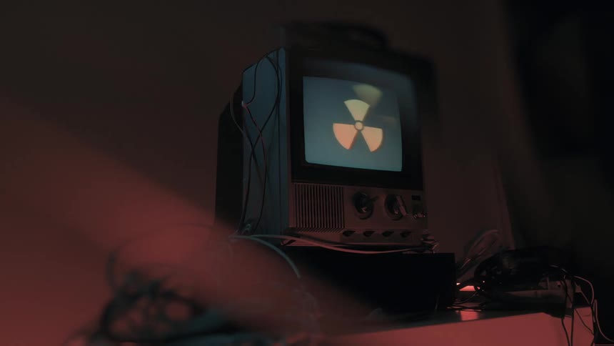 Angled view of an older model television with a glowing screen displaying a singlecolor signal surrounded by a tangle of cables illuminated by contrasting red and blue ambient lights