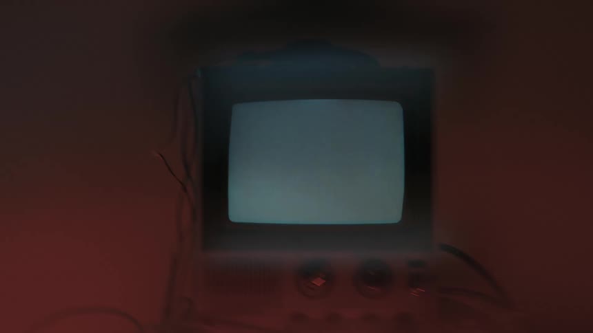 Small television in an area lit by colored lighting displays a series of white symbols on a blue background