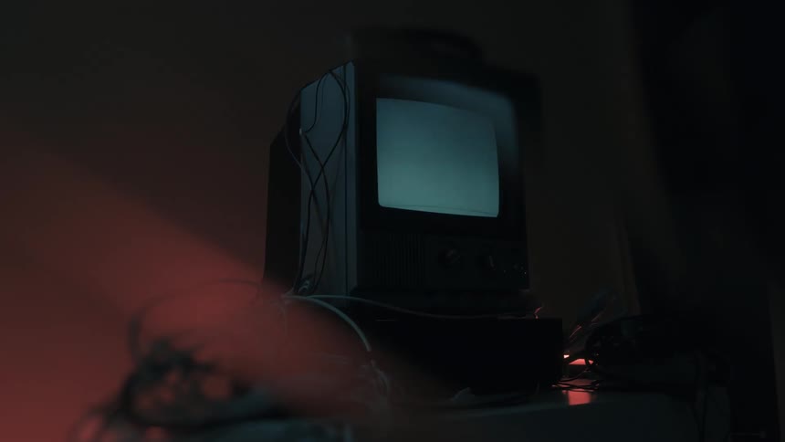 Angled view of an older model television with a glowing screen displaying a singlecolor signal surrounded by a tangle of cables illuminated by a red light
