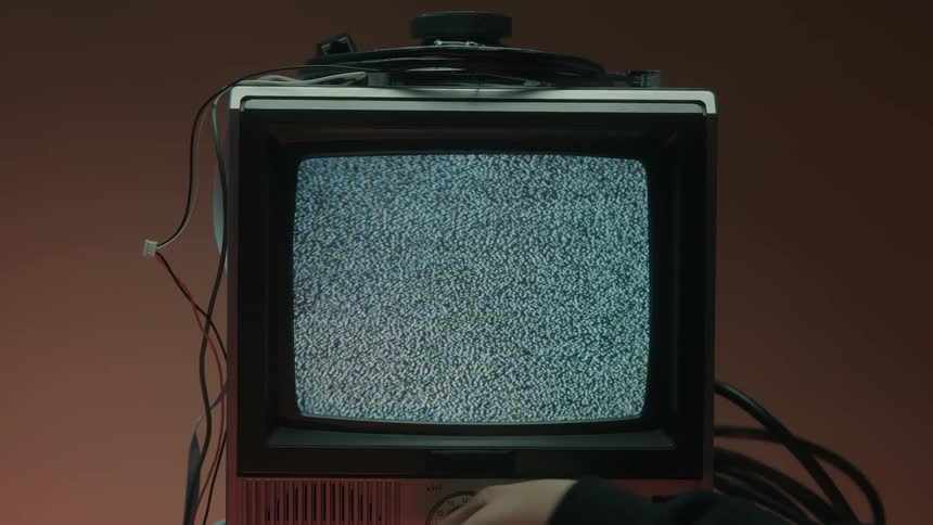 An older model television shows static on the screen while someone adjusts a knob