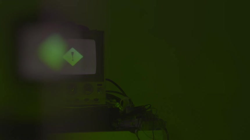 Angled view of an older model television set with a fully illuminated screen resting on a lower electronic device and a stand surrounded by cables and bathed in contrasting green and magenta ambient lights
