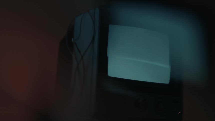 A shaky lowlight view of an old crt television set with a flickering screen showing symbols in a dark room
