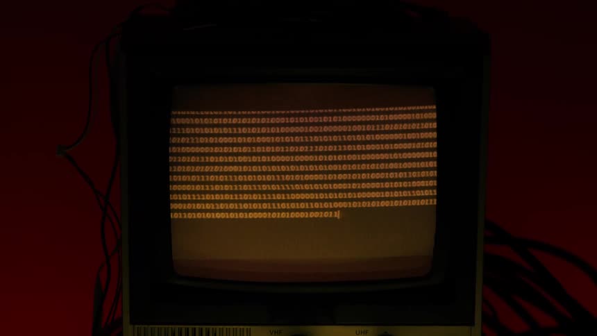 A vintage television screen displays lines of orange binary code being typed out against a dark background