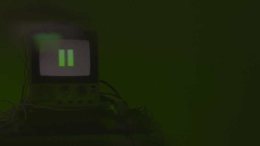 An older model television monitor with a continuously illuminated white screen resting on a lower electronic device with the entire setup surrounded by dark cables