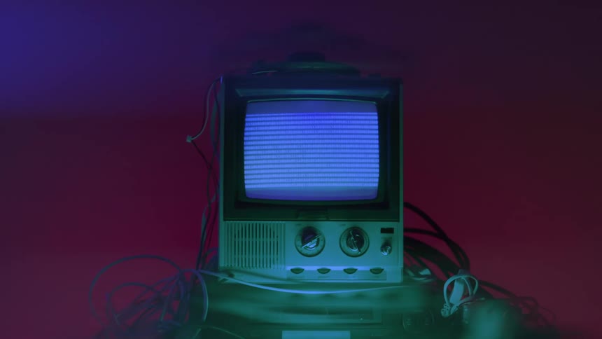 A retrostyle television set displaying a bluetinted screen full of moving visual noise sitting atop a lower device and surrounded by loose cables