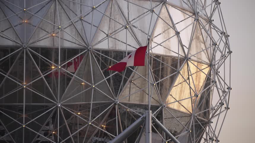 The canadian flag blows in the wind in front of the large sphere