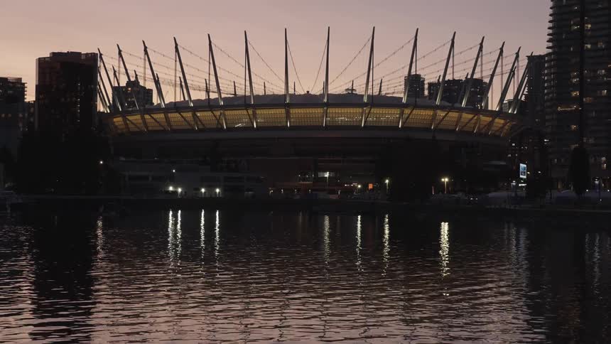 Stadium illuminated at dusk reflects its lights on the surrounding calm water