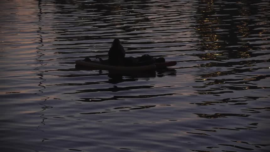 Two people sit in a boat floating on reflective water after dusk