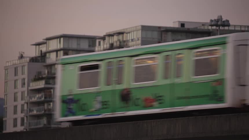 Modern midrise apartment buildings with glass balconies sit in the soft light of dusk as a train passes in the foreground