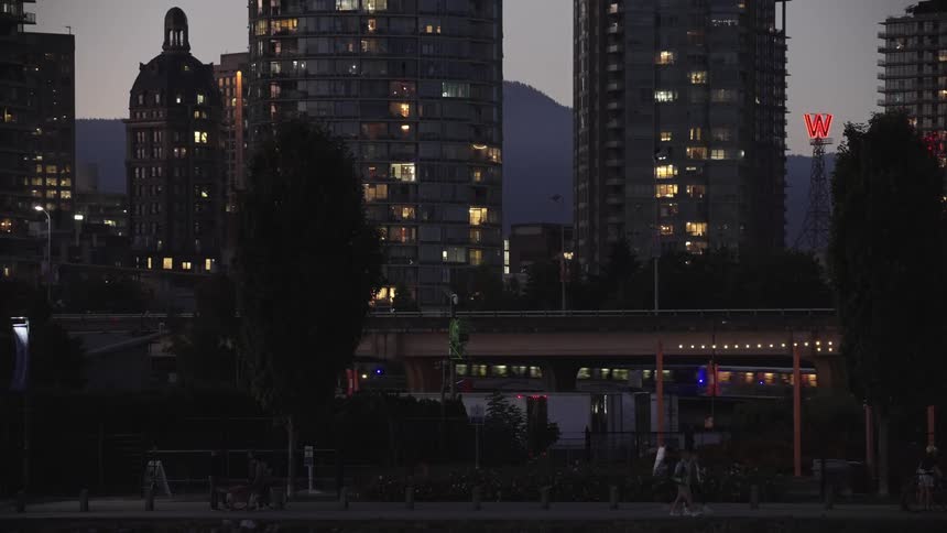 People walking at dusk with illuminated buildings in the background