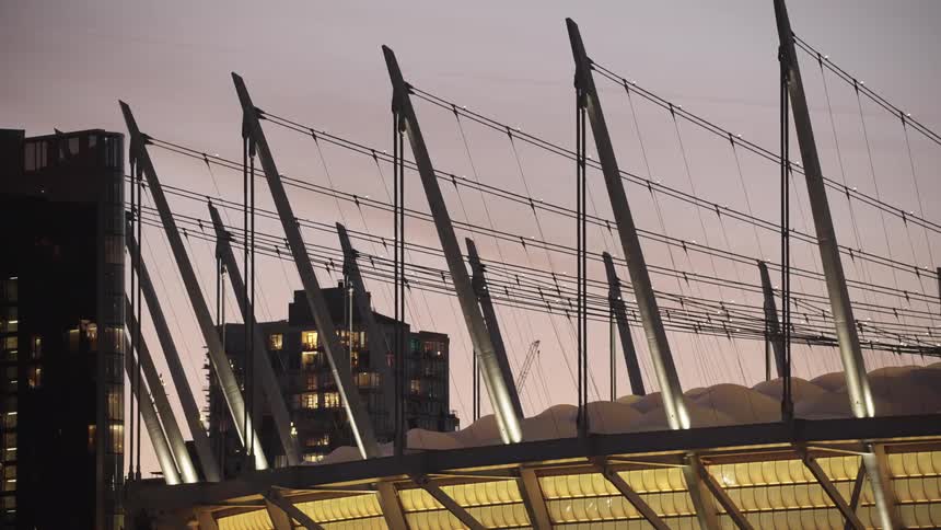 Cables run from the poles topping a stadium located near large residential high rises at dusk