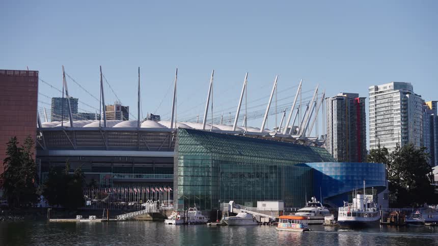 Passenger ferry travels through the water near a waterfront stadium on a summer day