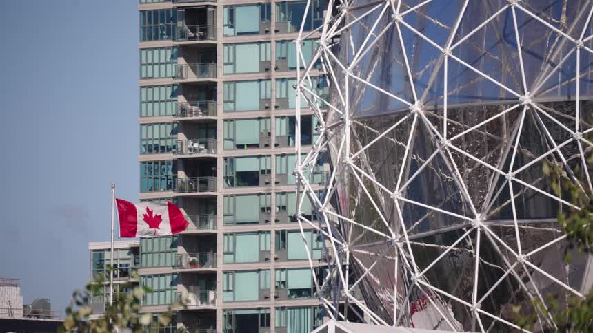 Large spherical structure covered in a network of struts stands next to a residential building and a canadian flag
