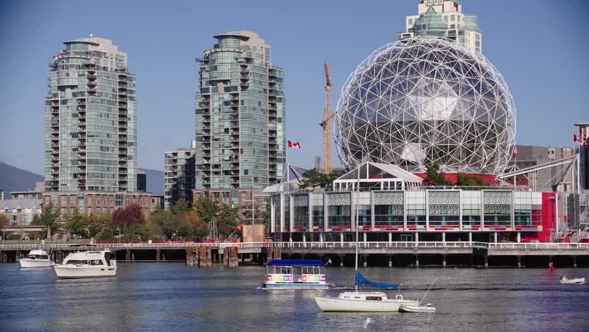 Boats sail near modern buildings and a metallic spherical structure by the waterfront