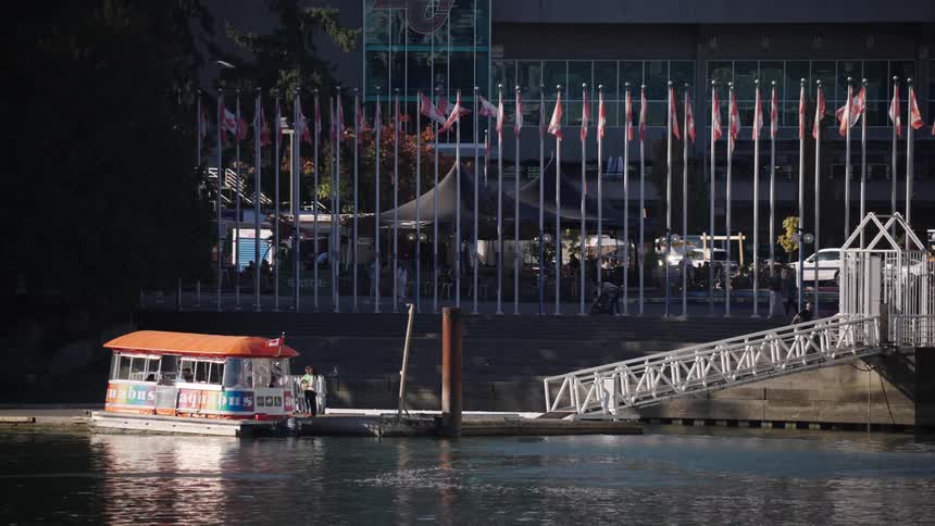 People walk down a gangway to board a ferry docked near a line of canadian flags