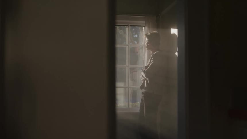 Man leaning against the wall watches thoughtfully as daylight enters through the window
