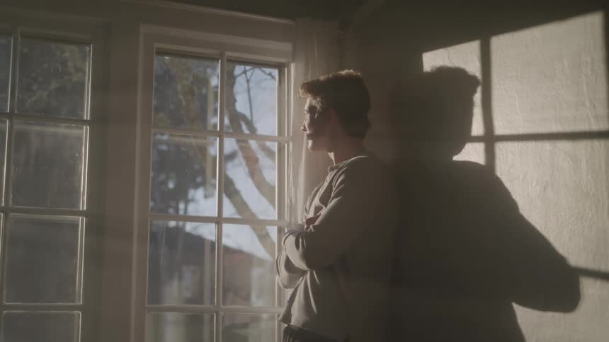 A man standing with his arms crossed and looking out a window composed of multiple panes