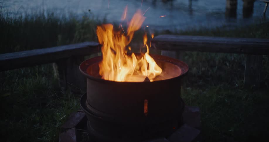 Bonfire burning outdoors near a lake at dusk