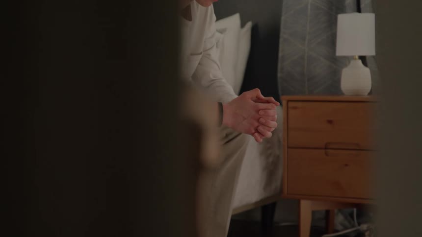 The man sits on the bed leaning forward