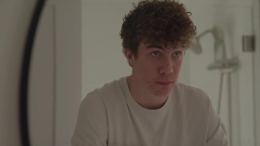 Young man staring at his reflection in the mirror in a bright room