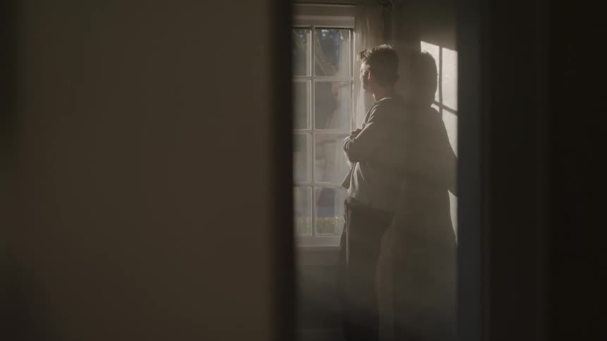 Man stands with arms crossed by a sunlit window