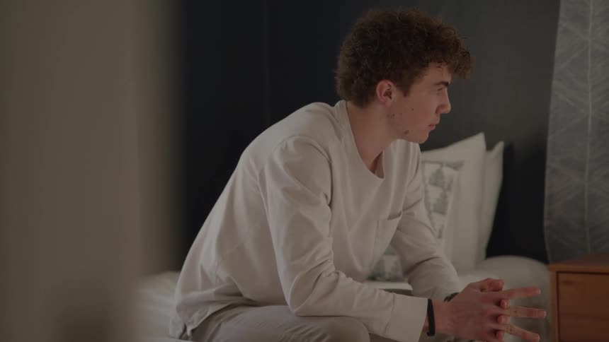 Man sitting on the edge of the bed looks thoughtfully to the side