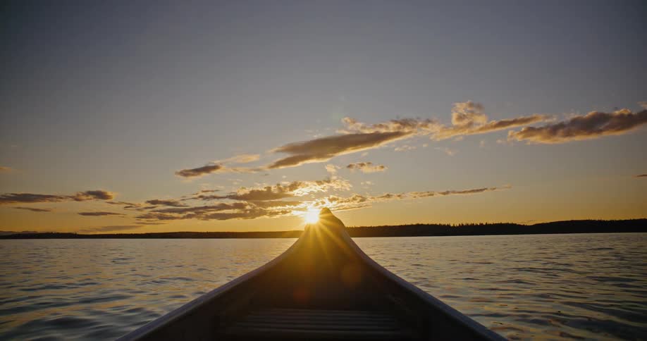 Canoe moves across calm waters at sunset under a partially lit sky
