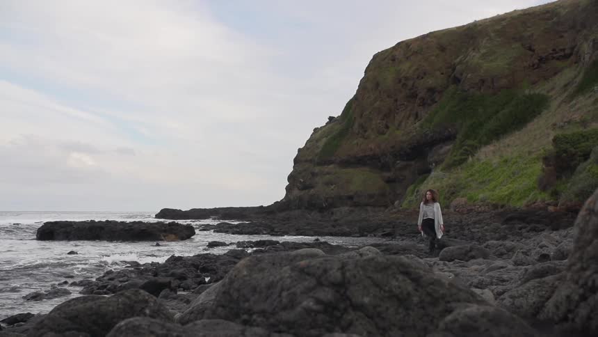Woman walking on some rocks by the shore