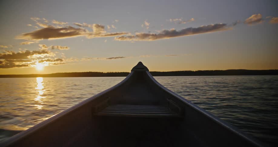 Canoe moves along the water at sunset toward a distant shoreline